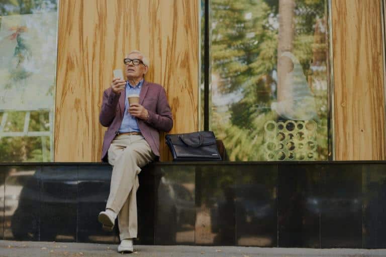 Homme assit dans la rue, regardant son téléphone et tenant un café