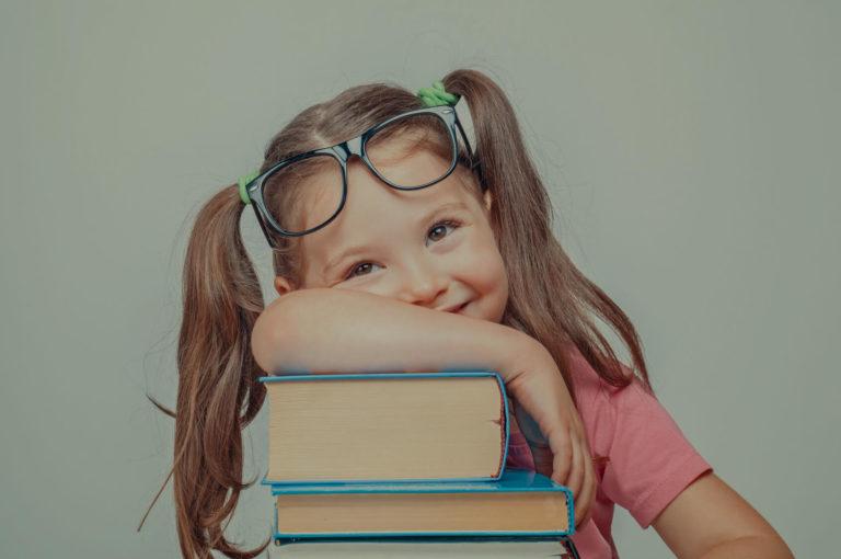 Petite fille portant des lunettes qui est accoudée sur une pile de livre