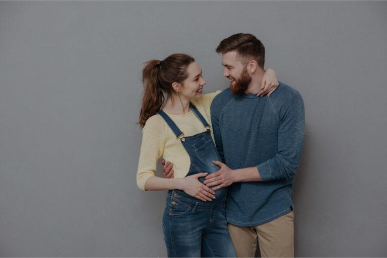 Homme heureux regardant sa femme et posant ses mains sur le ventre de sa femme enceinte