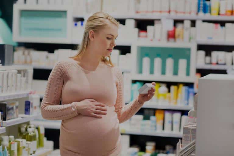 Femme blonde enceinte qui marche dans une pharmacie et qui regarde la boite d'un médicament