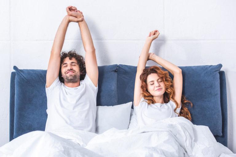 Couple d'homme et de femme assis dans leur lit et s'étirant les bras